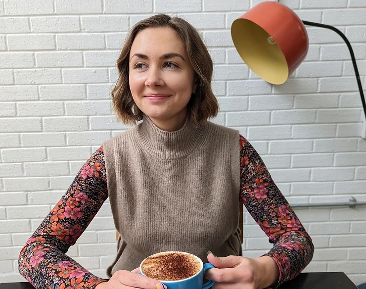 Photo of Alannah Wiseman sitting at a table smiling and holding a cup of coffee