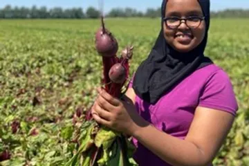 A girl in a farm field holds purple produce
